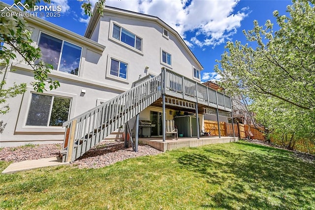back of property with a wooden deck, fence, a yard, stairs, and stucco siding