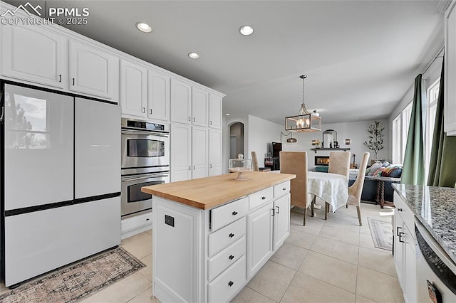 kitchen featuring wooden counters, stainless steel double oven, freestanding refrigerator, a notable chandelier, and light tile patterned flooring
