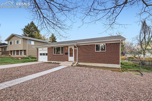 tri-level home with brick siding, fence, concrete driveway, an attached garage, and a shingled roof