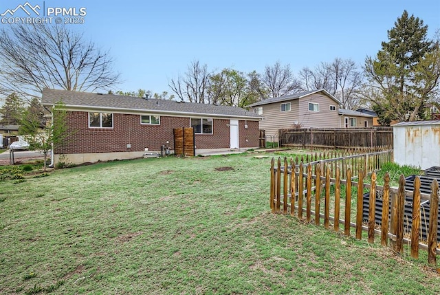 rear view of property with a fenced backyard, a yard, brick siding, a storage unit, and an outbuilding