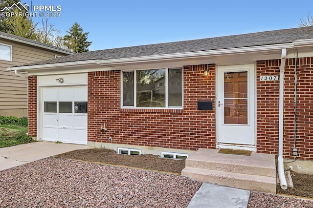 property entrance with brick siding, a shingled roof, an attached garage, and concrete driveway