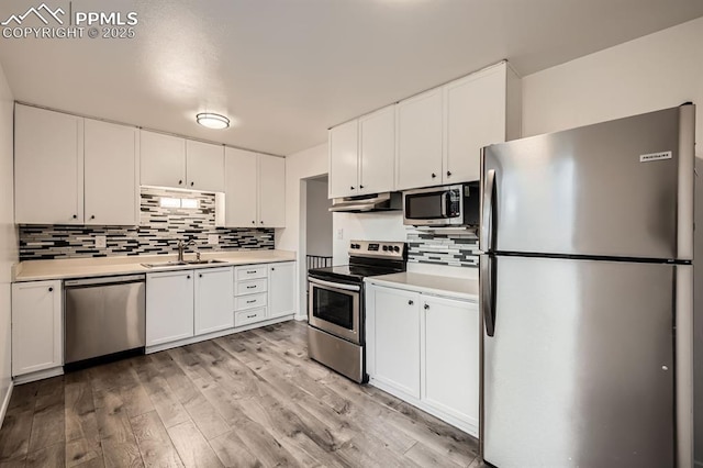kitchen with white cabinets, appliances with stainless steel finishes, light countertops, tasteful backsplash, and under cabinet range hood