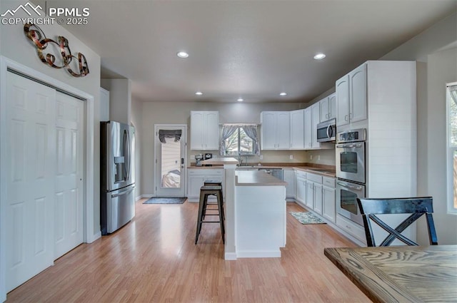 kitchen with a kitchen island, stainless steel appliances, light wood finished floors, and a breakfast bar area