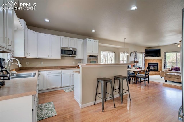 kitchen with a fireplace, a sink, white cabinets, a breakfast bar, and stainless steel appliances