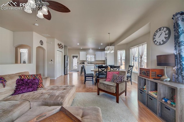 living area featuring light wood-type flooring, a ceiling fan, baseboards, and arched walkways
