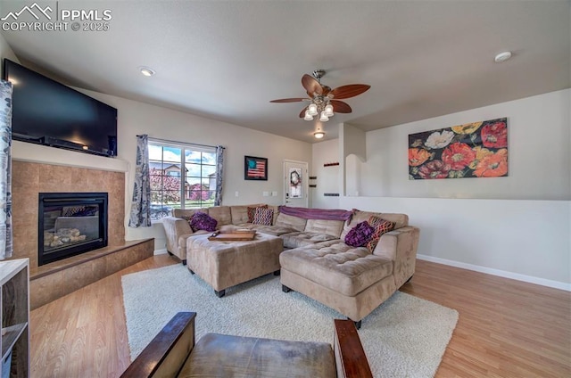 living room featuring baseboards, a high end fireplace, a ceiling fan, and wood finished floors