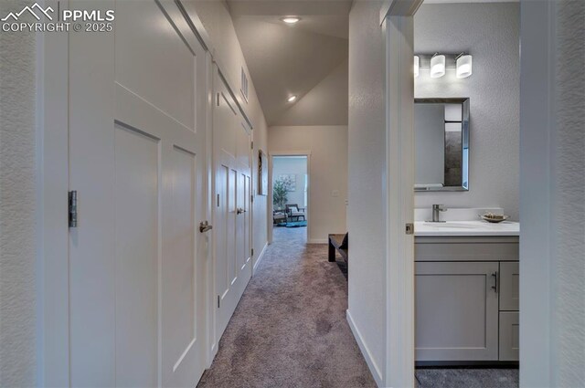 hall featuring carpet floors, visible vents, baseboards, a sink, and vaulted ceiling