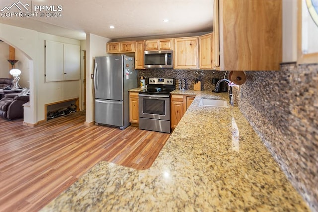 kitchen with decorative backsplash, arched walkways, light stone counters, a sink, and appliances with stainless steel finishes