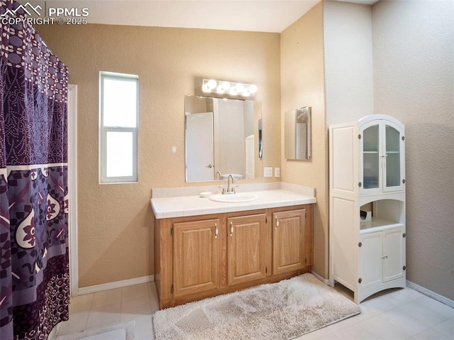 full bath featuring vanity, baseboards, a textured wall, and tile patterned floors