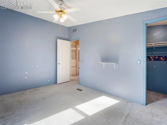 unfurnished bedroom with carpet floors, visible vents, a closet, a walk in closet, and ceiling fan