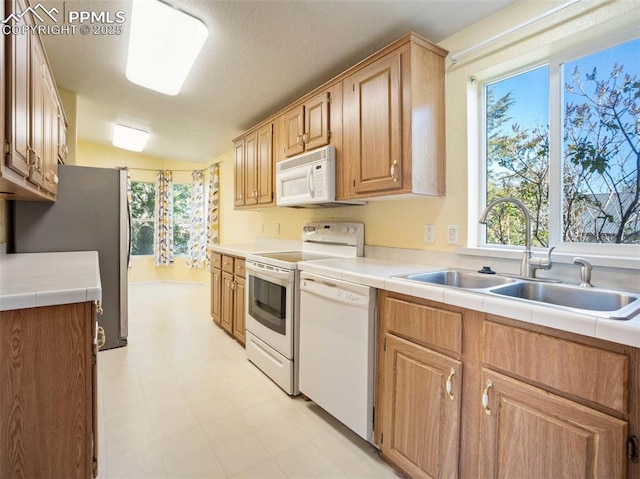 kitchen with a sink, tile counters, white appliances, and a healthy amount of sunlight