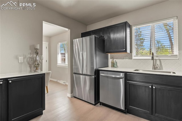 kitchen featuring light countertops, dark cabinetry, a sink, light wood-style flooring, and appliances with stainless steel finishes