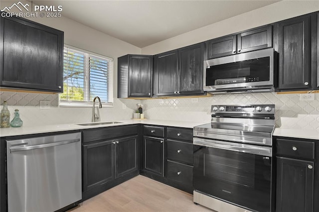 kitchen with appliances with stainless steel finishes, a sink, light countertops, light wood finished floors, and dark cabinetry