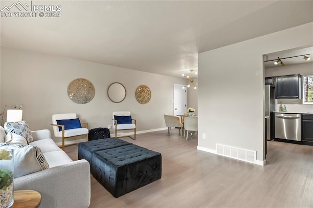 living room with baseboards, visible vents, and light wood-style flooring