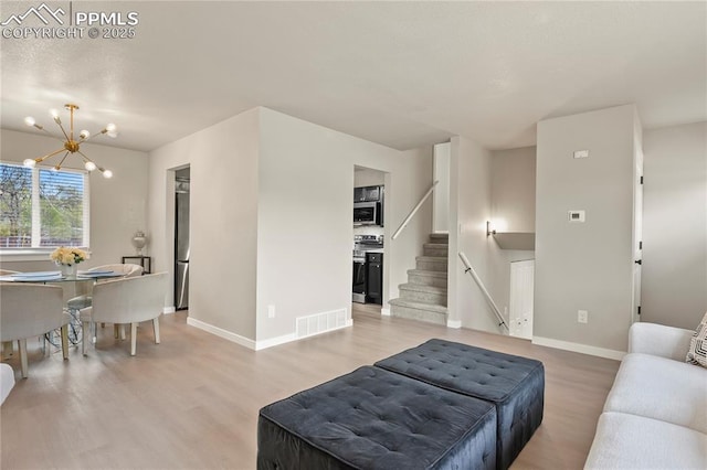 living area with an inviting chandelier, visible vents, light wood-style floors, baseboards, and stairway