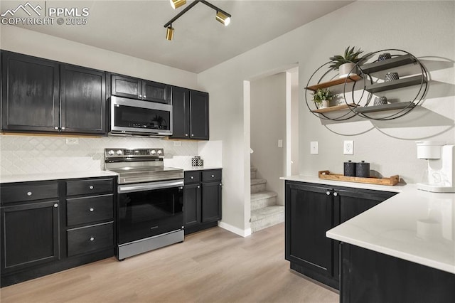 kitchen with decorative backsplash, appliances with stainless steel finishes, open shelves, dark cabinets, and light wood-style flooring