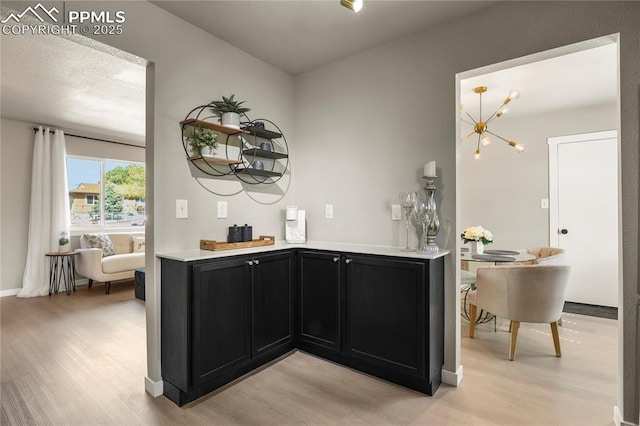 bar featuring baseboards, an inviting chandelier, bar, and light wood-style flooring