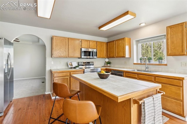 7665 Calloway Ct, Colorado Springs, CO 80919 - kitchen featuring appliances with stainless steel finishes, tile counters, a sink, light wood-type flooring, and a breakfast bar area