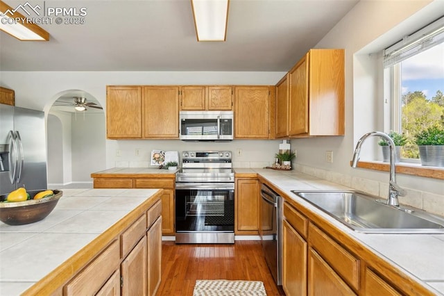 7665 Calloway Ct, Colorado Springs, CO 80919 - kitchen featuring appliances with stainless steel finishes, tile countertops, a sink, dark wood-style flooring, and arched walkways