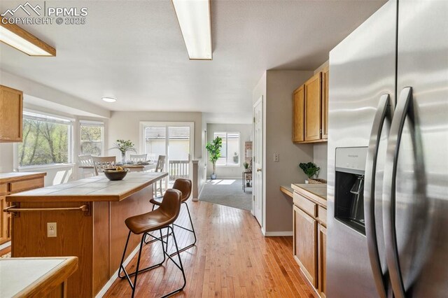 7665 Calloway Ct, Colorado Springs, CO 80919 - kitchen with stainless steel fridge with ice dispenser, tile countertops, a center island, light wood-type flooring, and a kitchen breakfast bar