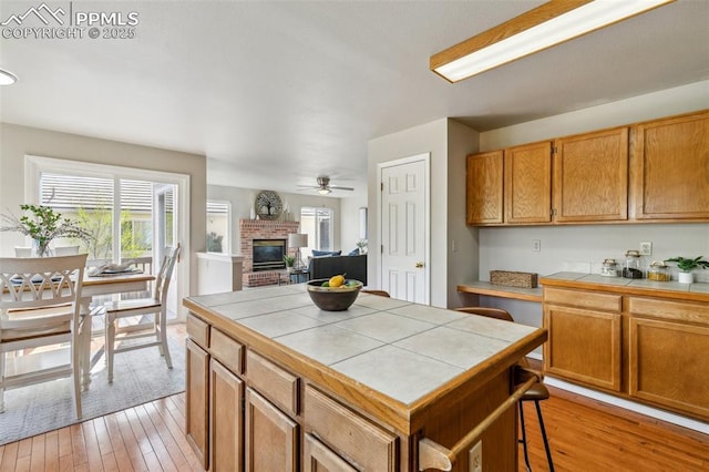 7665 Calloway Ct, Colorado Springs, CO 80919 - kitchen featuring tile counters, a fireplace, light wood-style floors, a ceiling fan, and a kitchen bar