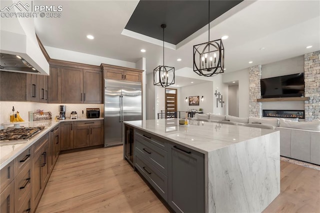 kitchen with a kitchen island, appliances with stainless steel finishes, light stone countertops, a chandelier, and custom range hood