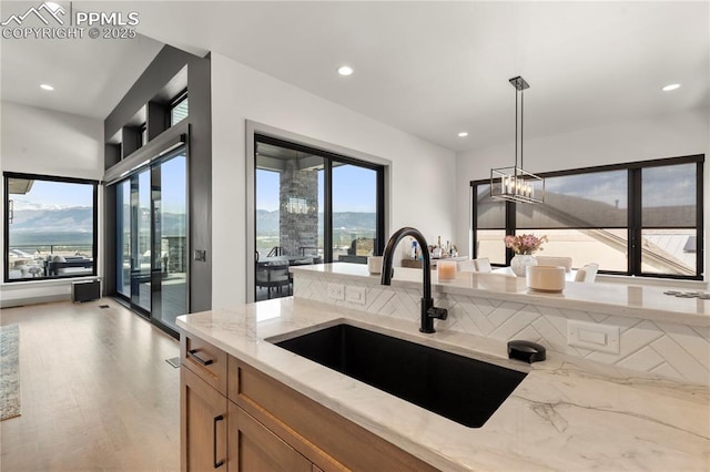 kitchen featuring brown cabinets, light stone counters, a sink, light wood-style flooring, and hanging light fixtures