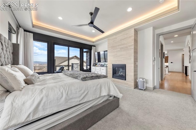 carpeted bedroom with recessed lighting, a raised ceiling, access to outside, and a fireplace