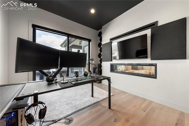 office space with baseboards, a glass covered fireplace, and wood finished floors
