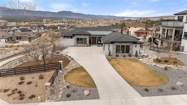 view of front facade featuring a residential view, fence, stone siding, a mountain view, and driveway