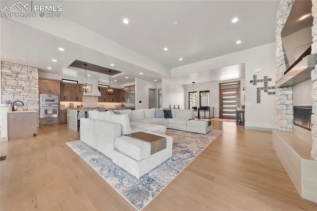 living room with light wood-style floors, a fireplace, a tray ceiling, and recessed lighting