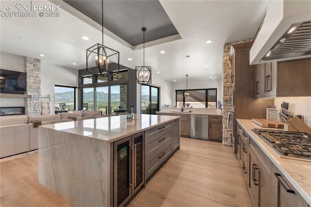 kitchen featuring wall chimney range hood, wine cooler, stainless steel appliances, recessed lighting, and light wood-style flooring
