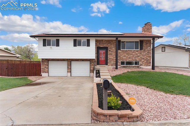 bi-level home with fence, a chimney, roof mounted solar panels, and a garage
