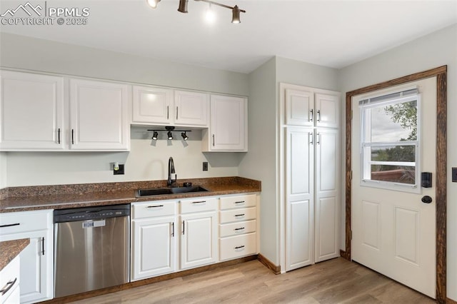 kitchen featuring light wood-type flooring, dark stone counters, white cabinets, a sink, and dishwasher
