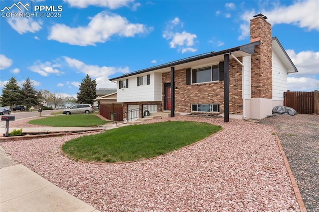 raised ranch with brick siding, fence, a front yard, and a chimney