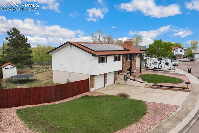 view of front of property with a chimney, roof mounted solar panels, a front lawn, concrete driveway, and an attached garage