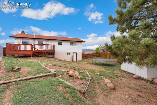 rear view of house with a trampoline, a deck, stairway, fence, and a yard