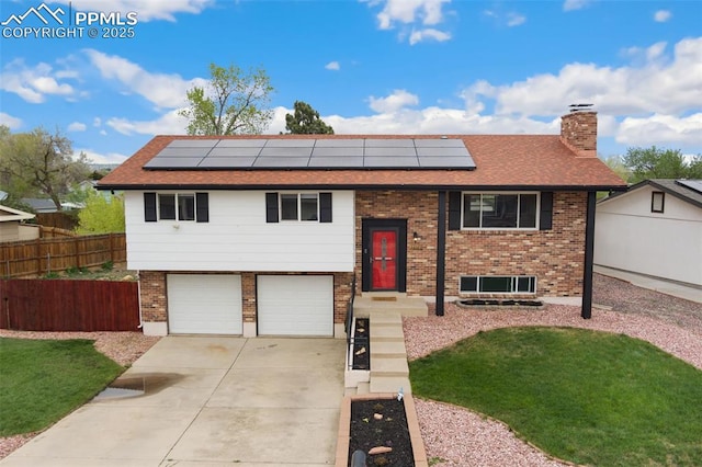 bi-level home with a garage, fence, a chimney, and solar panels