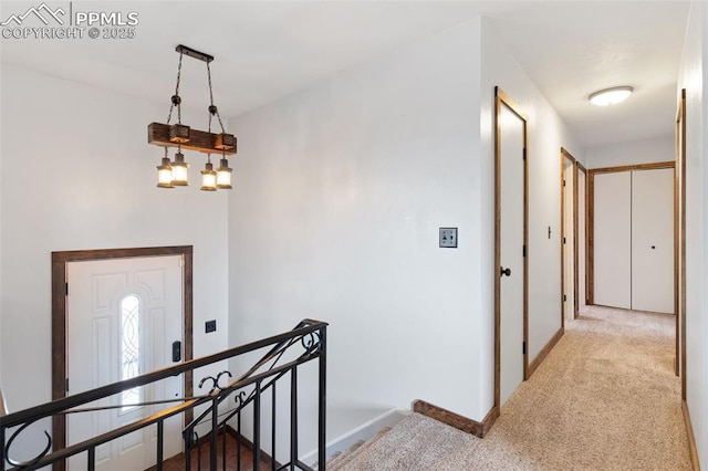 hallway featuring baseboards, an upstairs landing, and carpet