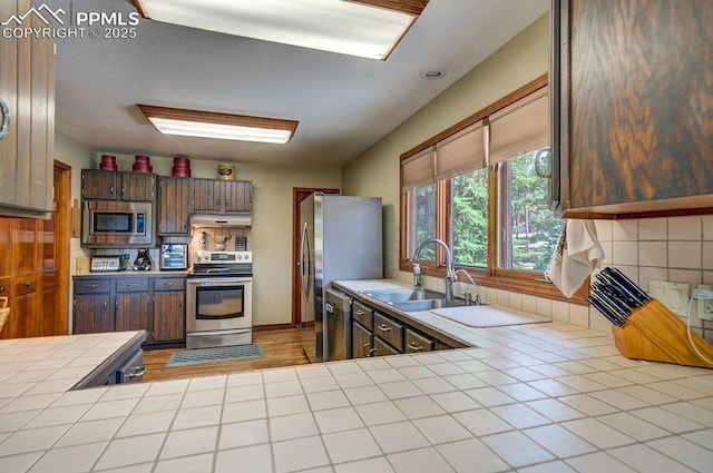 17815 Fairplay Way, Monument, CO 80132 - kitchen with appliances with stainless steel finishes, a sink, tile counters, tasteful backsplash, and under cabinet range hood