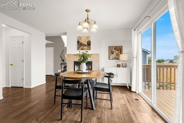 dining room with a tiled fireplace, visible vents, wood finished floors, and a chandelier