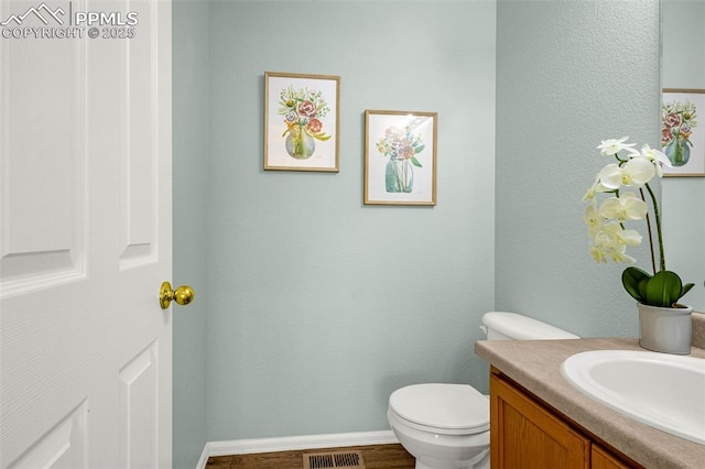 half bathroom with vanity, visible vents, wood finished floors, toilet, and baseboards