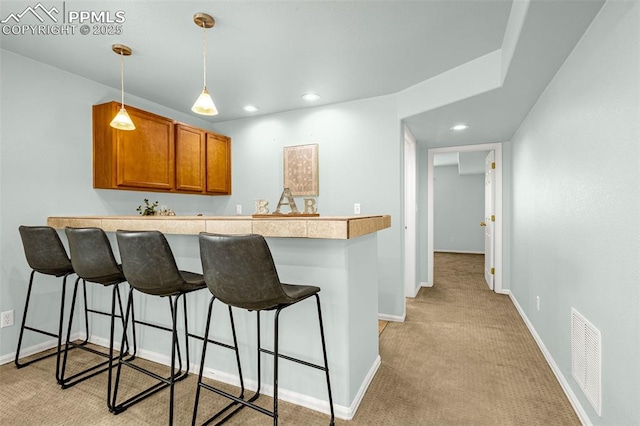 kitchen with a peninsula, a kitchen breakfast bar, light carpet, and brown cabinets