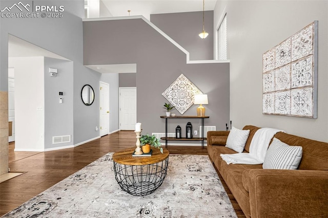 living room featuring baseboards, visible vents, wood finished floors, and a towering ceiling
