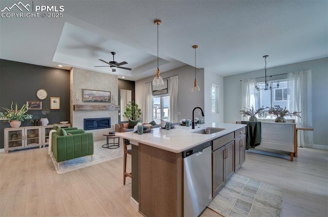kitchen with stainless steel dishwasher, a sink, light wood finished floors, and a tiled fireplace
