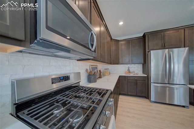 kitchen with light stone countertops, dark brown cabinetry, appliances with stainless steel finishes, light wood-type flooring, and backsplash