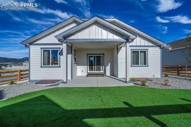 rear view of property with board and batten siding, a yard, fence, and a patio area