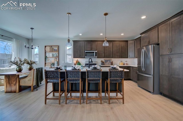 kitchen featuring dark brown cabinetry, appliances with stainless steel finishes, light countertops, light wood-style flooring, and tasteful backsplash