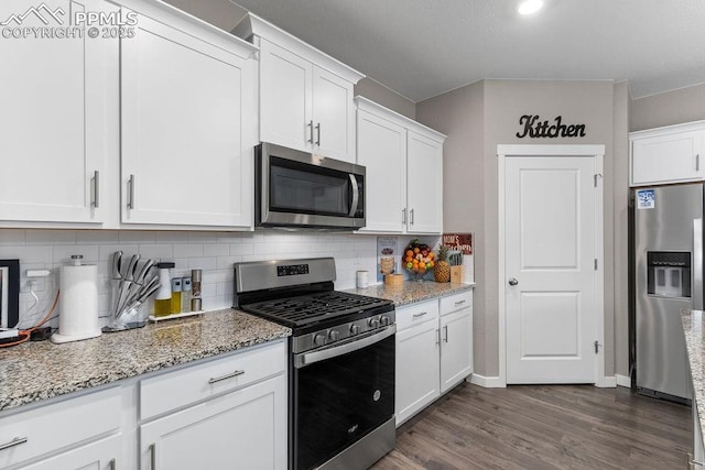 2186 Prairie Smoke Dr, Monument, CO 80132 - kitchen featuring white cabinets, appliances with stainless steel finishes, light stone counters, dark wood-type flooring, and backsplash