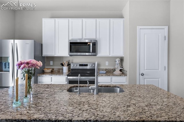 kitchen featuring a sink, appliances with stainless steel finishes, light stone counters, and white cabinetry